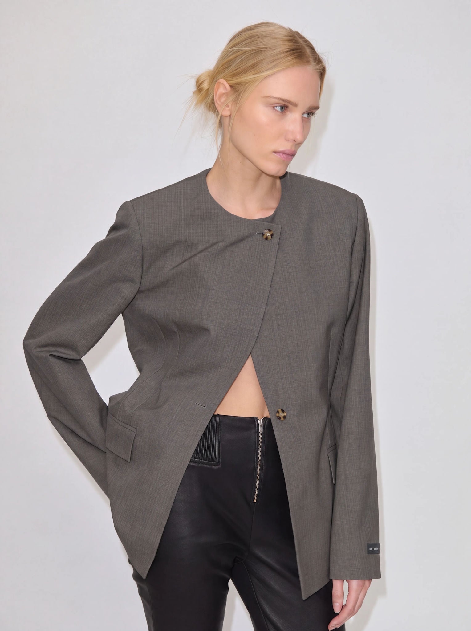 A person wears an open, collarless Robyn Fitted Blazer by Herskind ApS over black trousers.