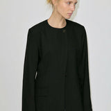 A woman wearing a Robyn Fitted Blazer, featuring a collarless tailored design with a buttoned front and structured shoulders.