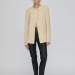 A model wearing a beige collarless Robyn Fitted Blazer by Herskind ApS with structured shoulders, black fitted trousers, and black pointed-toe flats.