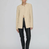 A model wearing a beige collarless Robyn Fitted Blazer by Herskind ApS with structured shoulders, black fitted trousers, and black pointed-toe flats.