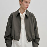 A person wearing a charcoal gray, cropped-length Stella Jacket by Herskind ApS over a white button-down shirt.