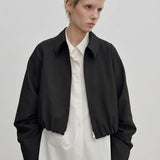 A person wearing a relaxed fit, cropped black Stella Jacket by Herskind ApS over a long-sleeved white button-down shirt.