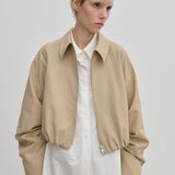 A person wearing a relaxed fit, cropped-length beige Stella Jacket by Herskind ApS with a wide collar over a white button-down shirt.