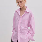 A person wears an oversized, light pink Jordan Shirt by Herskind ApS, featuring BCI cotton, a point collar, and a chest pocket.