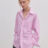 A person wears an oversized, light pink Jordan Shirt by Herskind ApS, featuring BCI cotton, a point collar, and a chest pocket.