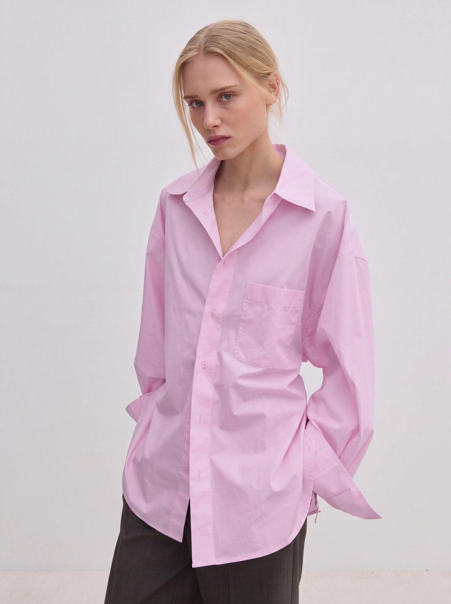 A person wears an oversized, light pink Jordan Shirt by Herskind ApS, featuring BCI cotton, a point collar, and a chest pocket.