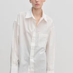 A person wears the oversized, long-sleeved white Jordan Shirt by Herskind ApS, featuring a breast pocket and a curved hem.