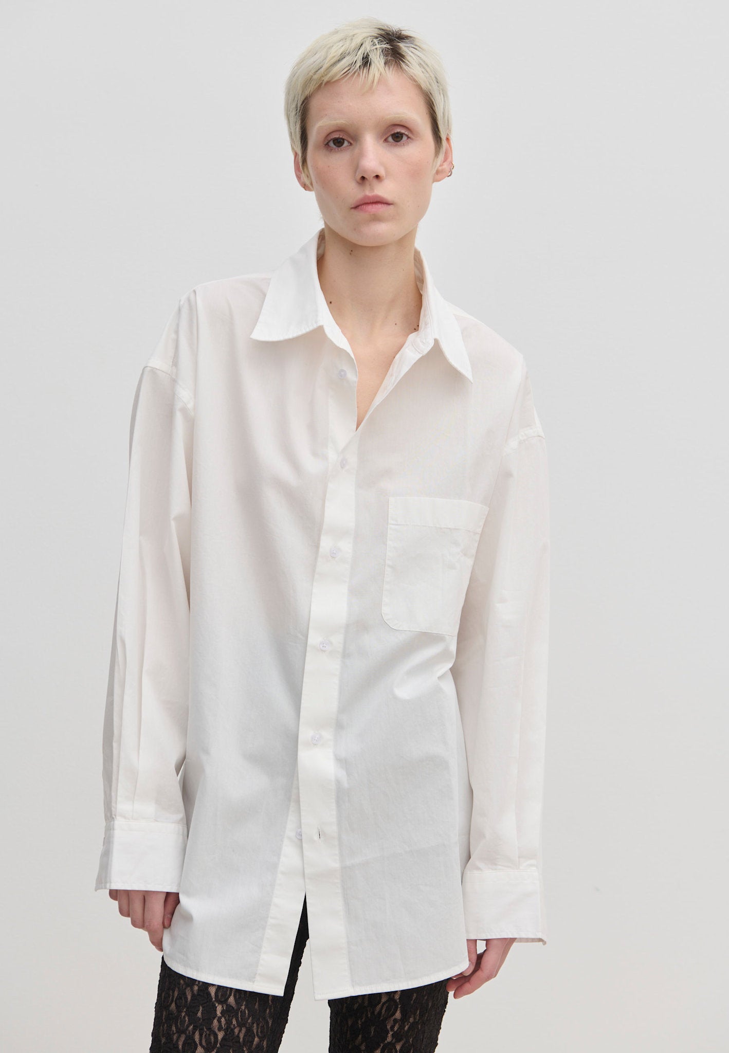 A person wears the oversized, long-sleeved white Jordan Shirt by Herskind ApS, featuring a breast pocket and a curved hem.