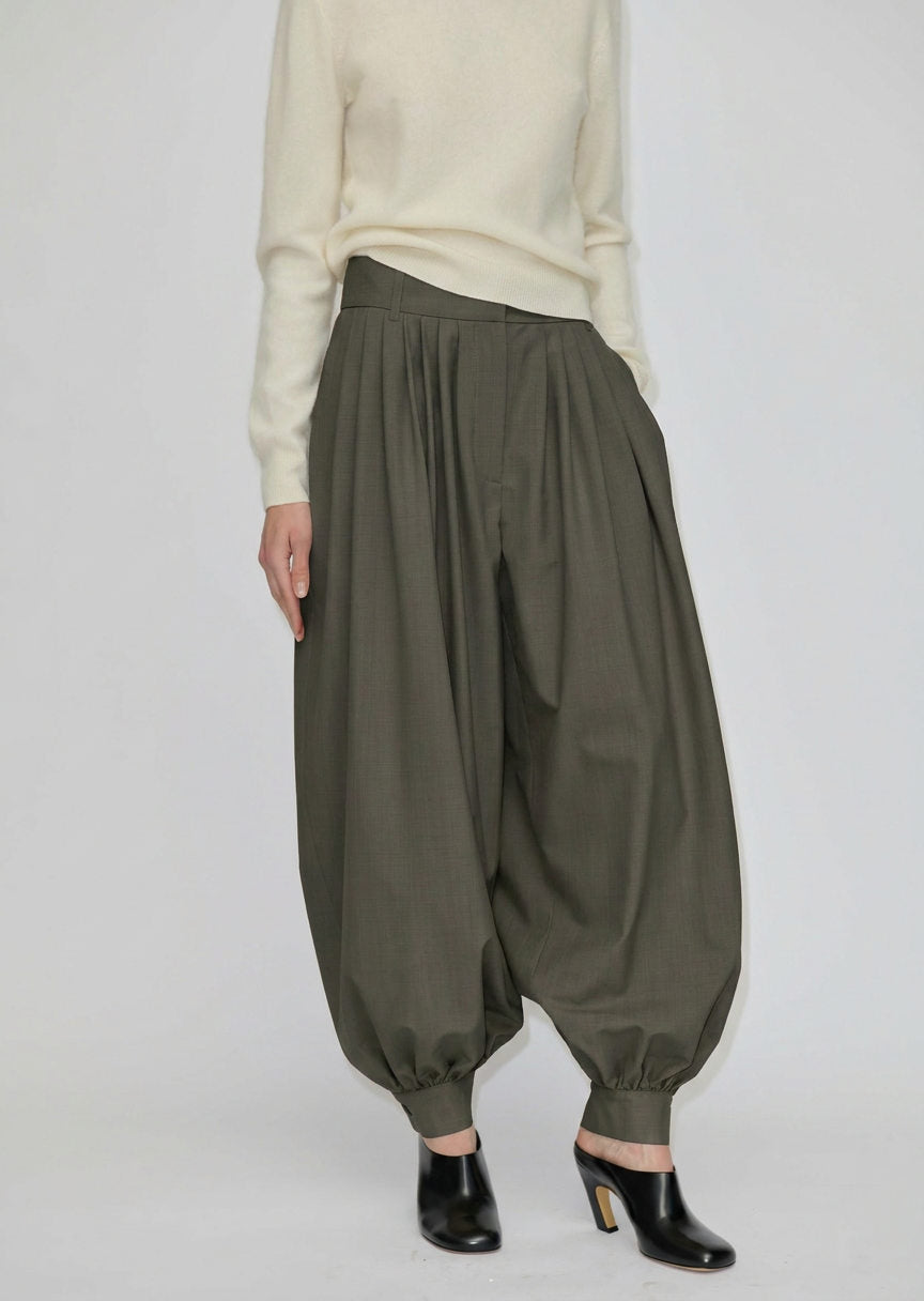 Herskind ApS Zeth High Waist Pants in olive green, featuring a high-waisted, relaxed, balloon-leg silhouette with gathered cuffs, worn with a cream sweater and black heeled mules.
