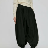 A person wearing black Zeth High Waist Pants with a balloon-leg silhouette, gathered hem, and black heeled mules.