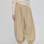 Herskind ApS Zeth High Waist Pants in khaki, featuring a high-waisted, pleated design with a relaxed fit and tapered, cuffed hem, worn with a cream sweater and black heeled mules.