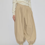 Herskind ApS Zeth High Waist Pants in khaki, featuring a high-waisted, pleated design with a relaxed fit and tapered, cuffed hem, worn with a cream sweater and black heeled mules.