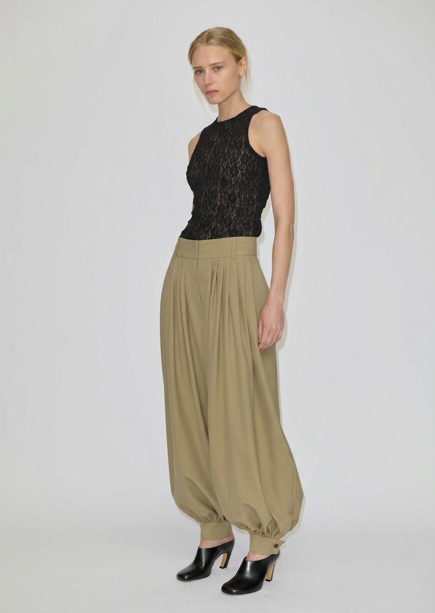 Zeth High Waist Pants by Herskind ApS in olive green with a relaxed, pleated balloon-leg silhouette and tapered cuffs, styled with a black lace sleeveless top and black heeled mules.