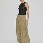 Zeth High Waist Pants by Herskind ApS in olive green with a relaxed, pleated balloon-leg silhouette and tapered cuffs, styled with a black lace sleeveless top and black heeled mules.
