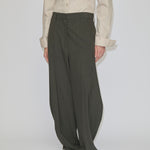 Person wearing a beige long-sleeved button-down shirt tucked into mid-waist, olive Dante Mid Waist Pants by Herskind ApS featuring a barrel leg shape with a slight taper at the hem and light-colored shoes.