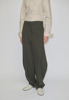 Person wearing a beige long-sleeved button-down shirt tucked into mid-waist, olive Dante Mid Waist Pants by Herskind ApS featuring a barrel leg shape with a slight taper at the hem and light-colored shoes.