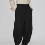A person wearing a beige button-down shirt and black Dante Mid Waist Pants, featuring a high-waisted, relaxed barrel leg fit with front pleats.