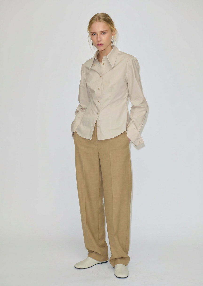 A person wearing a beige button-down shirt tucked into relaxed-fit, barrel leg Dante Mid Waist Pants by Herskind ApS and white shoes.