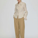 A person wearing a beige button-down shirt tucked into relaxed-fit, barrel leg Dante Mid Waist Pants by Herskind ApS and white shoes.