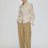 A person wearing a beige button-down shirt tucked into relaxed-fit, barrel leg Dante Mid Waist Pants by Herskind ApS and white shoes.
