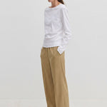 A person wearing a long-sleeved white shirt and Pinky Mid waist Pants, which are loose-fitting, wide-leg, beige trousers with an elasticated waistband.