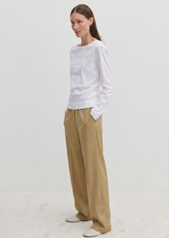 A person wearing a long-sleeved white shirt and Pinky Mid waist Pants, which are loose-fitting, wide-leg, beige trousers with an elasticated waistband.