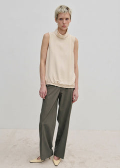 A person wearing a sleeveless cream-colored mock-neck top and Herskind ApS Ivano Mid waist Pants in grey.