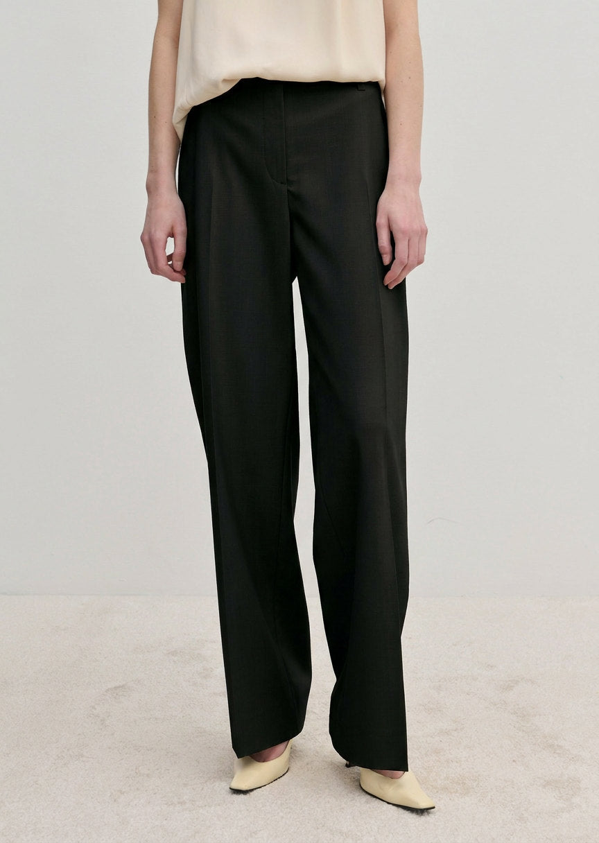 Ivano Mid waist Pants by Herskind ApS in black, featuring a mid-waist, straight-leg fit, and pressed creases, worn with a cream top and light-colored shoes.