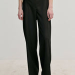 Ivano Mid waist Pants by Herskind ApS in black, featuring a mid-waist, straight-leg fit, and pressed creases, worn with a cream top and light-colored shoes.
