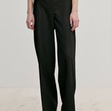 Ivano Mid waist Pants by Herskind ApS in black, featuring a mid-waist, straight-leg fit, and pressed creases, worn with a cream top and light-colored shoes.