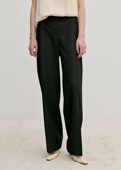 Ivano Mid waist Pants by Herskind ApS in black, featuring a mid-waist, straight-leg fit, and pressed creases, worn with a cream top and light-colored shoes.