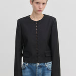 Herskind ApS Marge Fitted Blazer: a black collarless cropped blazer with a front row of fabric-covered buttons, worn over blue jeans.