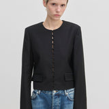 Herskind ApS Marge Fitted Blazer: a black collarless cropped blazer with a front row of fabric-covered buttons, worn over blue jeans.