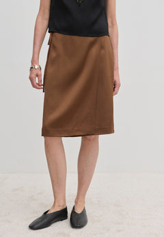A brown knee-length A-line Emmy Wrap Skirt by Herskind ApS, worn with a black top and black slip-on shoes.