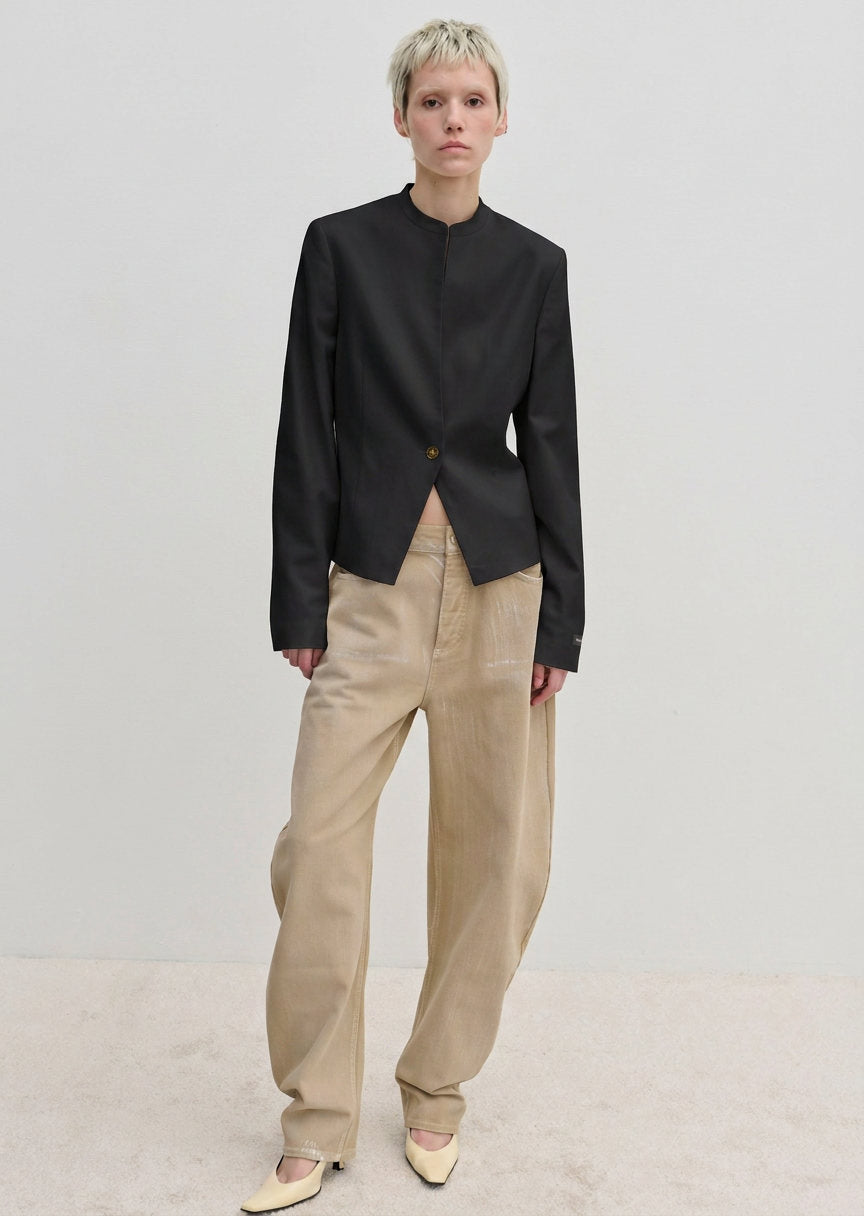 A person wearing a fitted, dark, single-button, stand-collar Henry Fitted Blazer by Herskind ApS with light tan wide-leg jeans and pale yellow pointed-toe shoes.