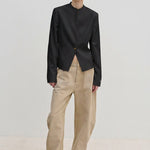 A person wearing a fitted, dark, single-button, stand-collar Henry Fitted Blazer by Herskind ApS with light tan wide-leg jeans and pale yellow pointed-toe shoes.