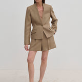 A woman wears a tan tailored blazer with a single button and matching Reggy High Waist Shorts by Herskind ApS, paired with light-colored pointed-toe heels.