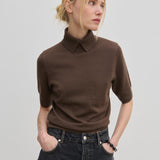 A person wears a short-sleeved brown merino wool Perry Knit Blouse by Herskind ApS with a collared neckline tucked into dark gray jeans.