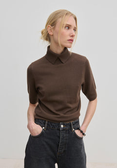 A person wears a short-sleeved brown merino wool Perry Knit Blouse by Herskind ApS with a collared neckline tucked into dark gray jeans.