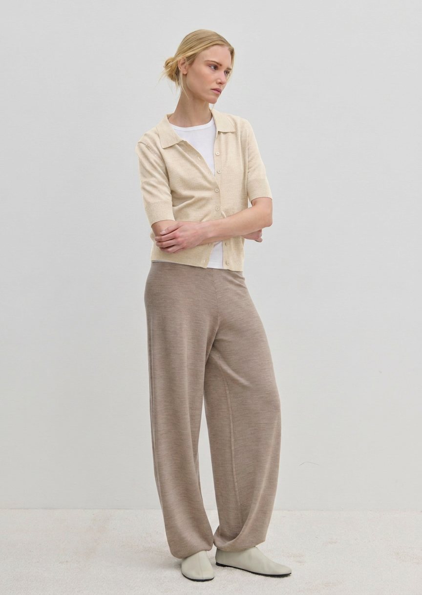 A person wearing a Kaspar Knit Polo from Herskind ApS over a white t-shirt, paired with wide-leg trousers and light-colored shoes.