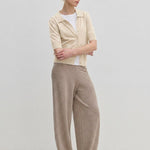 A person wearing a Kaspar Knit Polo from Herskind ApS over a white t-shirt, paired with wide-leg trousers and light-colored shoes.