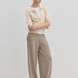 A person wearing a Kaspar Knit Polo from Herskind ApS over a white t-shirt, paired with wide-leg trousers and light-colored shoes.
