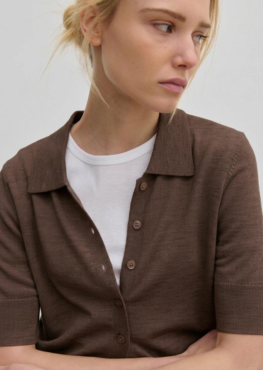 A person wearing a brown Kaspar Knit Polo by Herskind ApS, buttoned over a white crew-neck t-shirt.