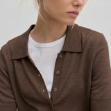 A person wearing a brown Kaspar Knit Polo by Herskind ApS, buttoned over a white crew-neck t-shirt.