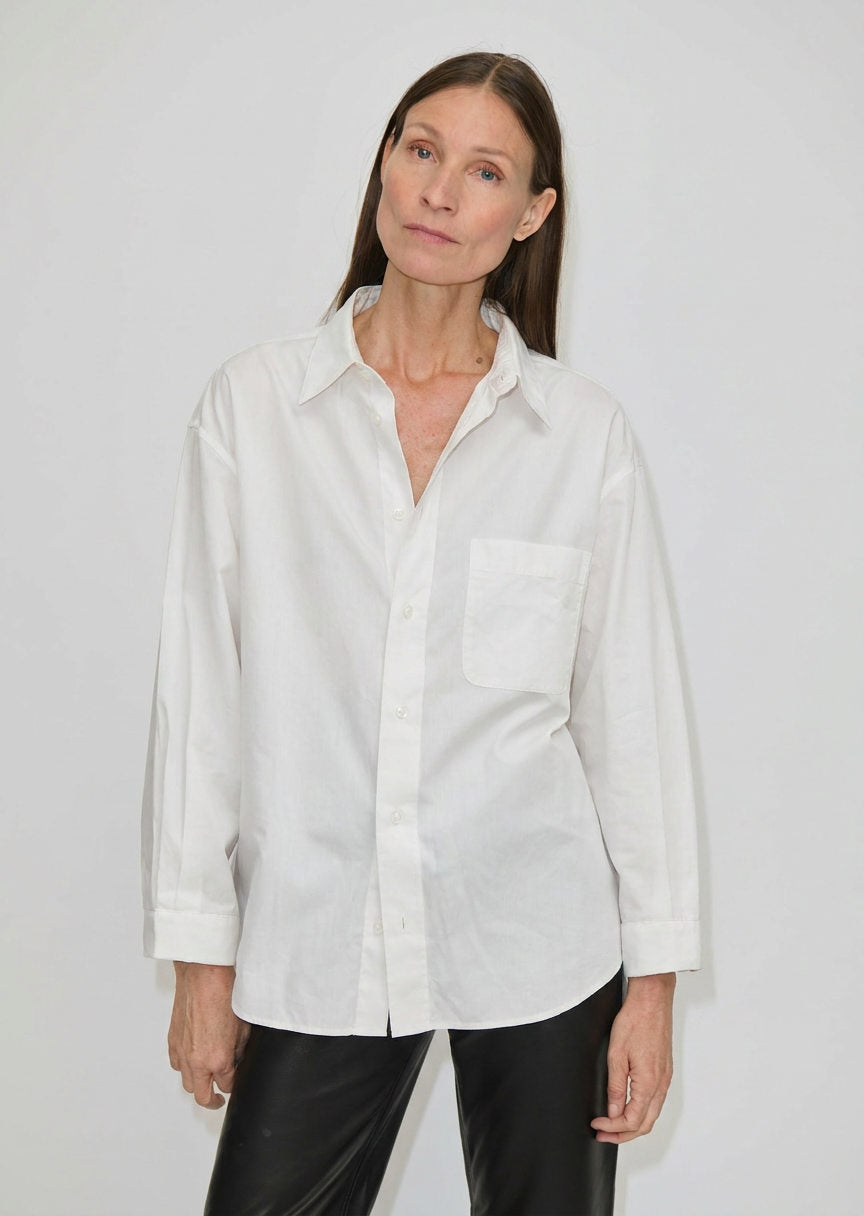 A person wearing a white, relaxed fit Lorenzo Shirt by Herskind ApS featuring a point collar and a chest pocket.