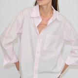 A person wearing a pale pink, relaxed fit Lorenzo Shirt by Herskind ApS, featuring a point collar, long sleeves, and a chest pocket.
