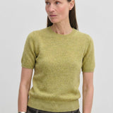A woman wearing a lime green Thora Knit Blouse tucked into dark trousers with a thin belt.