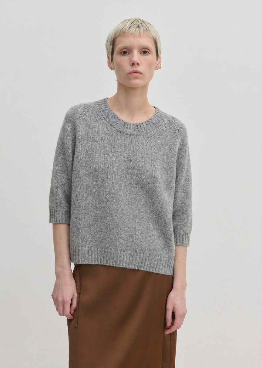 A person wearing a grey Josie Cashmere Knit Blouse with a relaxed-fit, crew-neck, and elbow-length sleeves, paired with a brown skirt.