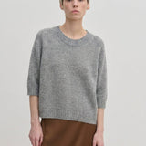 A person wearing a grey Josie Cashmere Knit Blouse with a relaxed-fit, crew-neck, and elbow-length sleeves, paired with a brown skirt.
