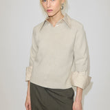 A person wears a beige Herskind ApS Josie Cashmere Knit Blouse layered over a collared shirt with cuffs visible at the sleeves.